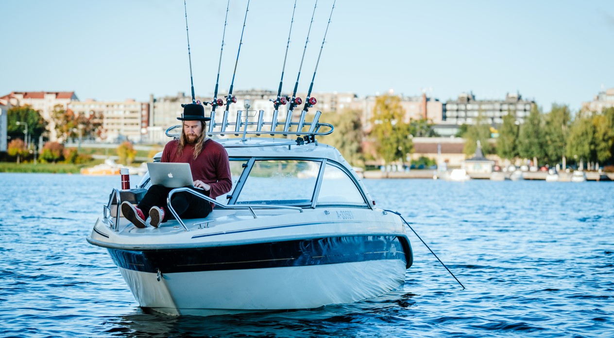 Mies tietokoneen kanssa veneen kannella, taustalla Mikkelin satama.