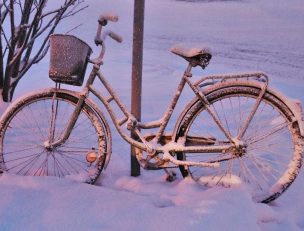 Polkupyörä nojaamassa liikennemerkkiin lumisessa maisemassa.