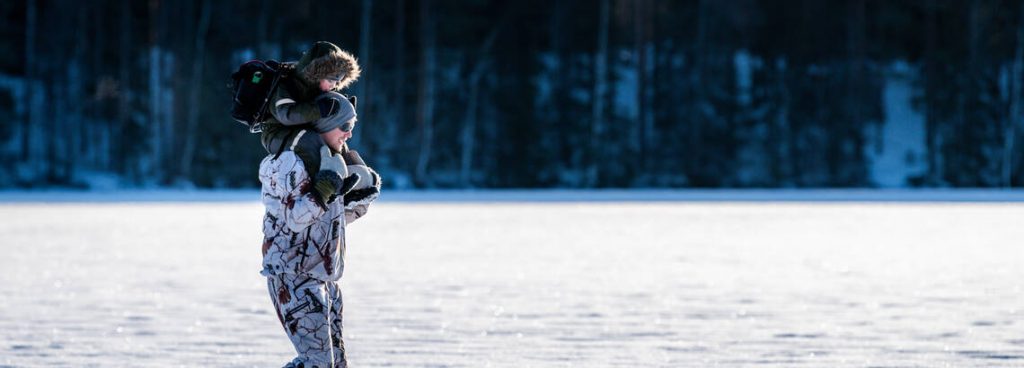 Mies kantaa lasta harteillaan talvisessa maisemassa.