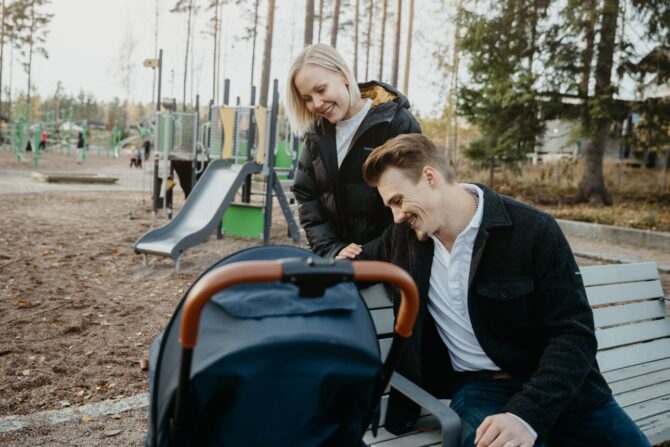 Nainen ja mies lastenvaunujen kanssa leikkipuistossa.