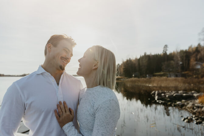 Mies ja nainen järven rannalla, taustalla rantamaisemaa ja vettä.