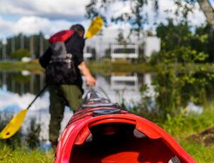 Henkilö vetämässä kanoottia lammelle, taustalla Mikaelin rakennus.