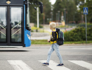Lapsi kävelemässä suojatiellä, taustalla linja-auto.