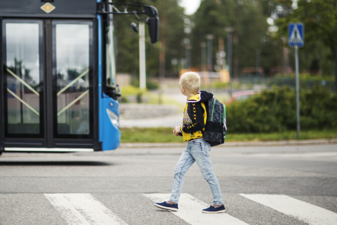 Lapsi kävelemässä suojatiellä, taustalla linja-auto.