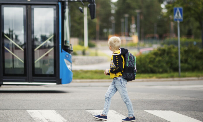 Lapsi kävelemässä suojatiellä, taustalla linja-auto.